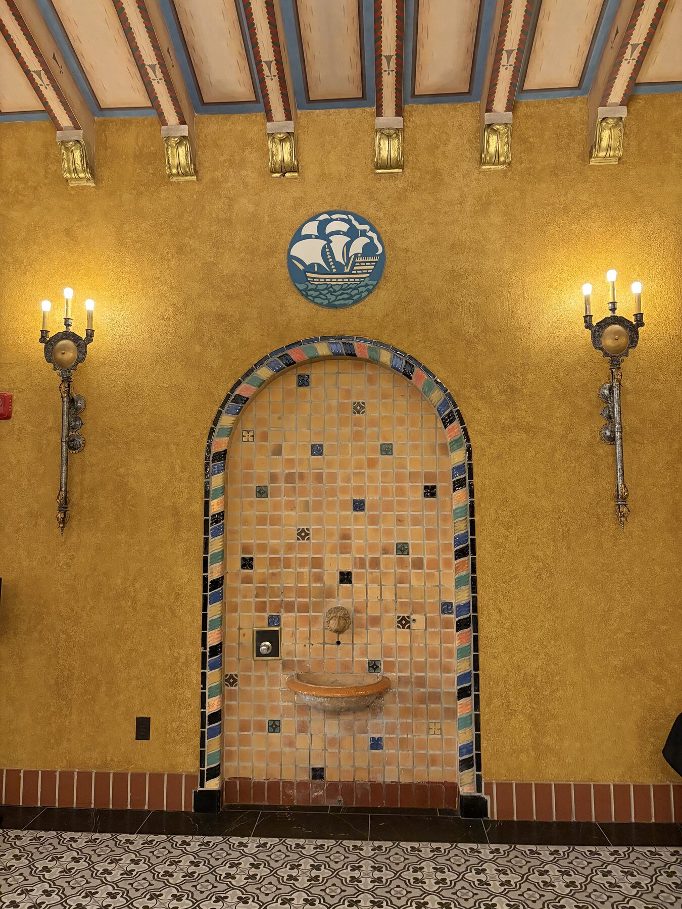 A restored tile fountain between two wall sconces in the lobby